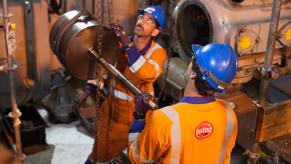 Two Entec workers move a piston rod to a compressor cylinder